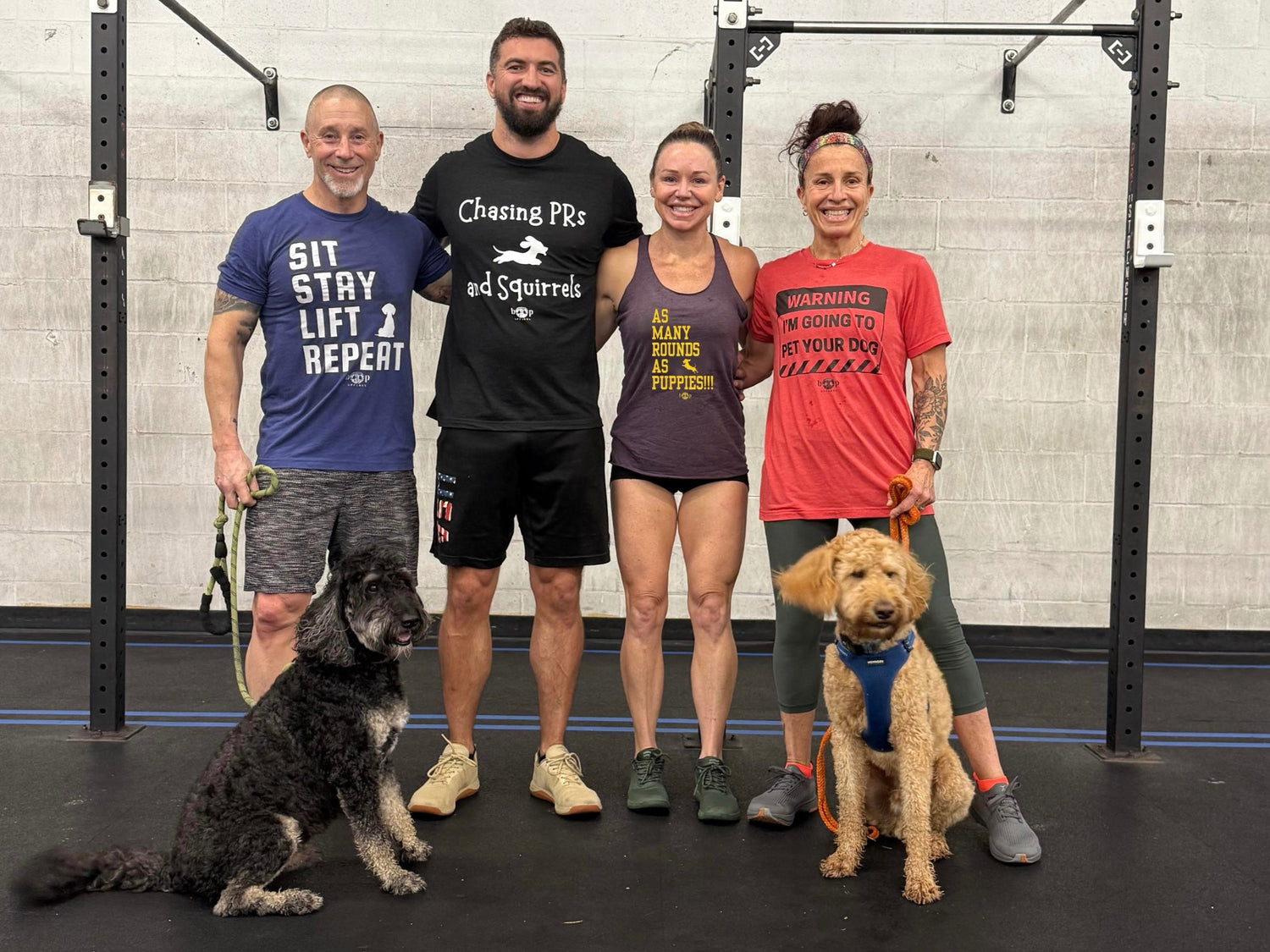 Four people and two dogs posing in a gym setting