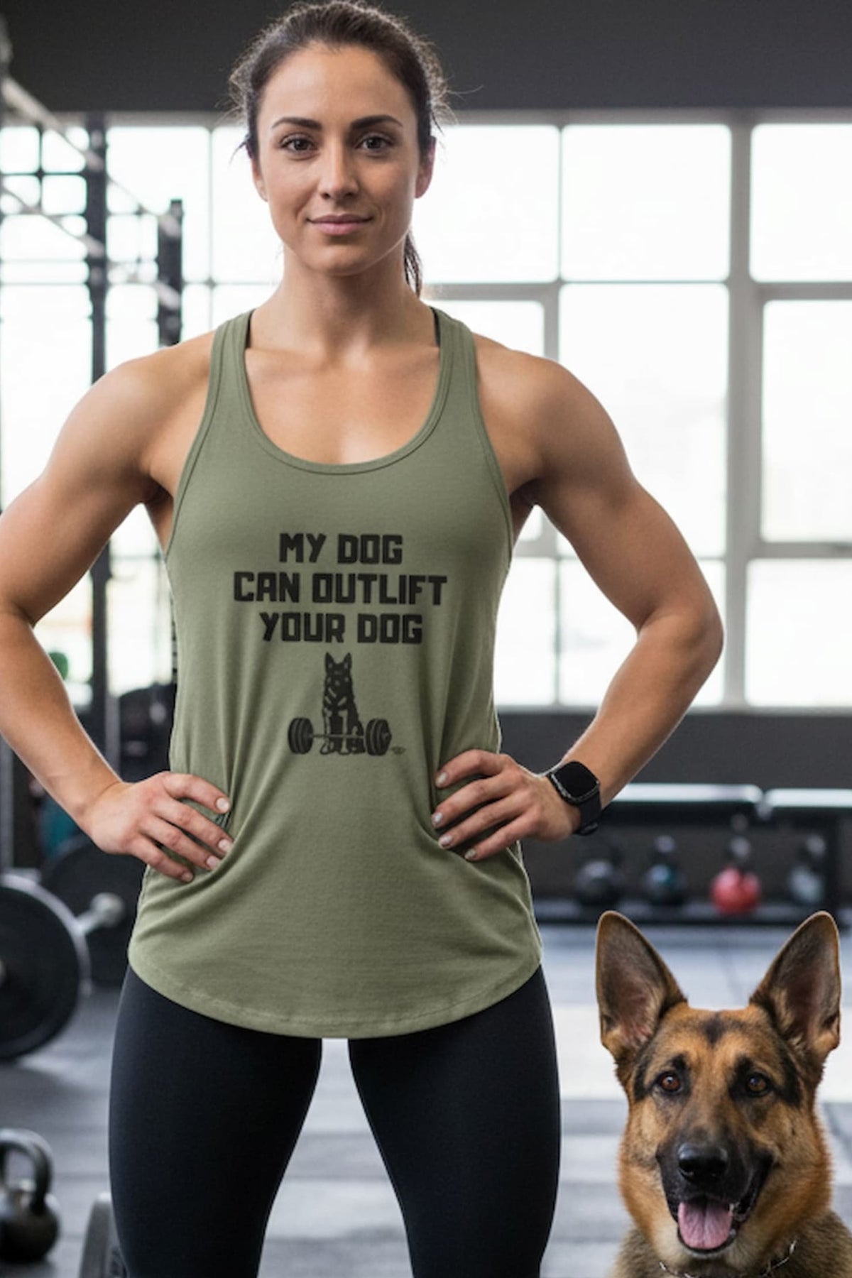 A woman in a gym wearing an olive green racerback tank top with the text 'MY DOG CAN OUTLIFT YOUR DOG' and a dog graphic, standing next to a German Shepherd dog.